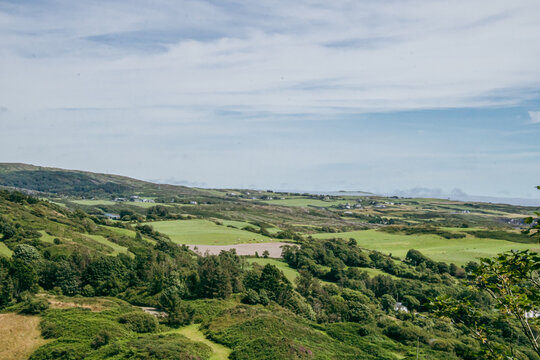 Scenic view of lush green hills, fields, and countryside under a cloudy blue sky