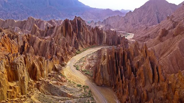Aerial view of a winding dirt road through rugged yellow canyon ridges in the Red Mountain Stone Forest, Kuqa, Xinjiang, China