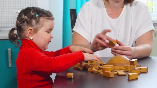 A Caucasian mother and daughter share a playful learning activity with wooden blocks at home. The scene illustrates family bonding, creative thinking, early education, and Montessori principles. Side 