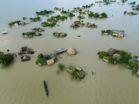 Aerial view of a flooded village with houses on small islands of land surrounded by muddy water and a small boat with people in Rajshahi District, Rajshahi Division, Bangladesh.
