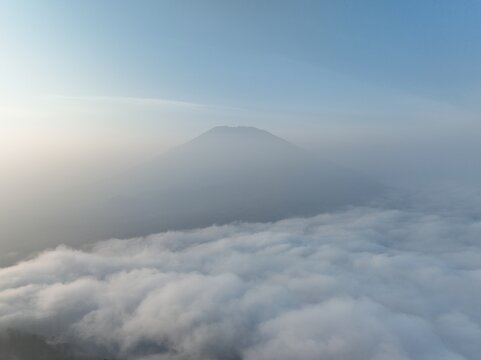 Aerial view of Mount Telomoyo rising above a thick blanket of clouds during a soft morning light in Kecamatan Ngablak, Jawa Tengah, Indonesia.
