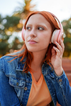 Young woman listening to music on pink headphones outdoors, showing individuality and relaxed lifestyle