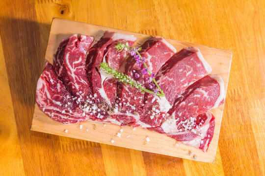 Slices of raw beef arranged on a wooden board with herbs and salt