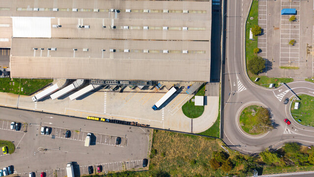 Aerial view of the Esselunga Spa logistics facility featuring loading docks with trucks, a large warehouse building, and an adjacent roundabout in Sesto Ulteriano, Lombardia, Italy.