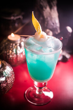 Colorful cocktail served in a glass with ice and a fruit garnish, placed on a red surface