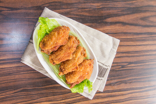 Fried chicken wings served on a plate with lettuce on a wooden table