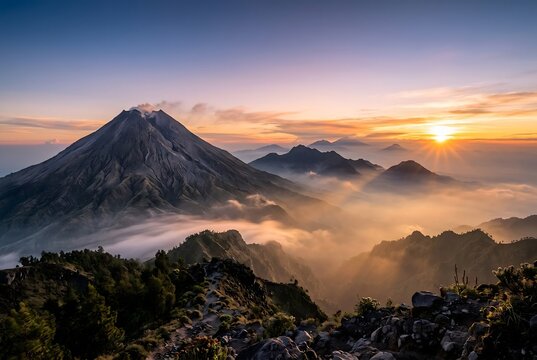 A breathtaking wide angle photography view of Mount Merapi volcano during a majestic sunrise with golden mist rolling over layered mountain ridges in Yogyakarta, Indonesia.