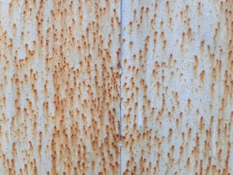 Close up texture of rust streaks and corrosion on old white metal surface. Grunge industrial background with orange rust spots and weathered pattern