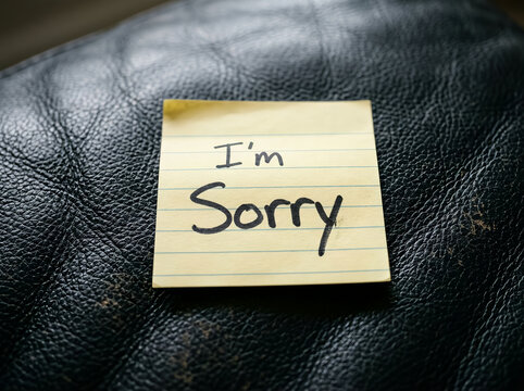 A yellow sticky note with the handwritten message im sorry placed on a textured black leather surface