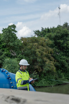 Male engineer checks water management infrastructure beside large pipeline and canal during routine sluice gate inspection and drainage system maintenance.