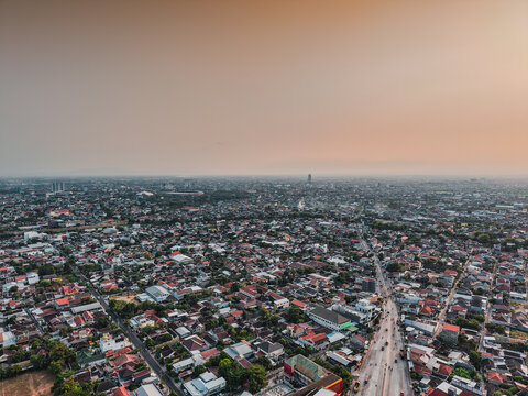 Aerial view of the dense urban landscape of Surakarta with its characteristic rooftops, winding streets, and hazy sunset sky in Surakarta, Jawa Tengah, Indonesia.