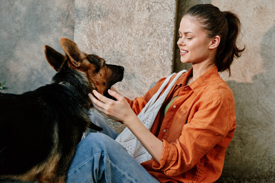 Smiling woman in an orange shirt sits on the floor, petting a German Shepherd. Close-up of warm interaction between person and dog, showing trust, joy, and a strong daily bond.