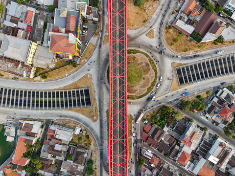 Aerial view of Jembatan Kereta Api Joglo, a prominent red railway bridge spanning over a busy roundabout in the urban landscape of Surakarta, Jawa Tengah, Indonesia.