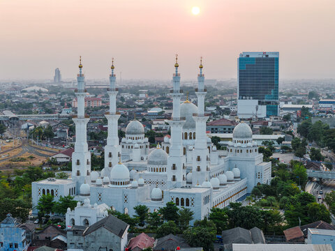 Aerial view of Sheikh Zayed Grand Mosque with its white domes and minarets surrounded by the urban landscape at sunset in Surakarta, Central Java, Indonesia.