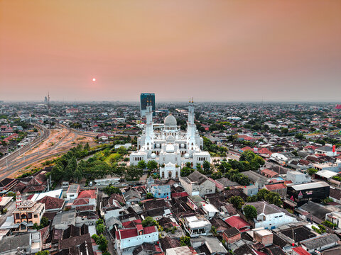 Aerial view of Sheikh Zayed Grand Mosque surrounded by dense urban rooftops and greenery at sunset in Surakarta, Central Java, Indonesia.