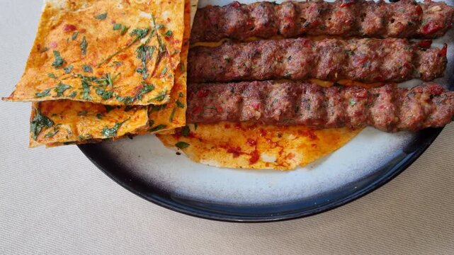 Delicious traditional Turkish Adana Kebab rotating on a plate with grilled vegetables and pita bread
