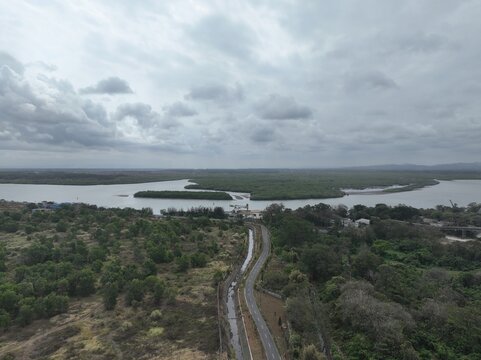Aerial view of the coastal landscape with mangrove forests, a winding road, and a river estuary in Cilacap, Central Java, Indonesia.