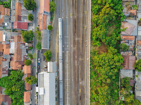 Aerial view of Stasiun Kejaksan with a train on the tracks, surrounded by urban rooftops and lush green trees in Cirebon, West Java, Indonesia.