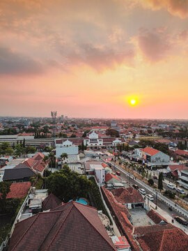 Aerial view of Stasiun Kejaksan surrounded by urban rooftops and streets during a vibrant sunset in Cirebon, West Java, Indonesia.