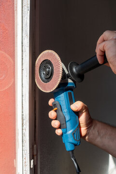 Man holding an angle grinder with a flap disc to restore a wooden window frame