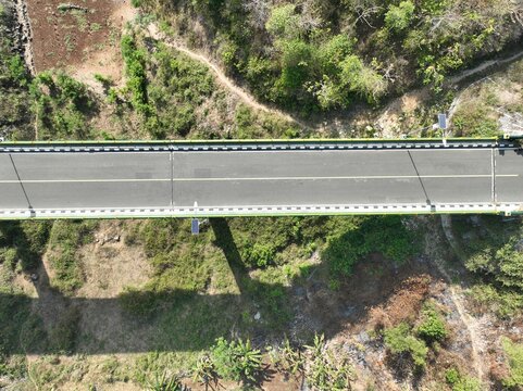 Aerial view of a bridge spanning a lush green valley with dense vegetation and trees in Gunungkidul Regency, Special Region of Yogyakarta, Indonesia.
