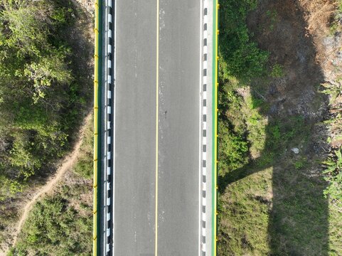 Aerial view of a bridge with yellow and black-white railings surrounded by lush green vegetation in Gunungkidul Regency, Special Region of Yogyakarta, Indonesia.