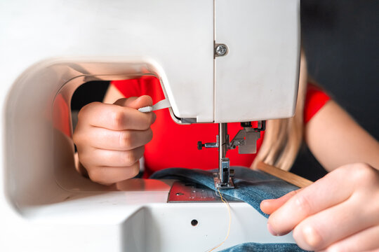 Woman repairing and upcycling jeans with a sewing machine and fabric patch, illustrating circular fashion, visible mending, slow fashion, textile reuse and sustainable DIY.