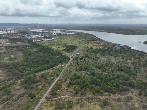 Aerial view of the industrial landscape featuring a river, storage tanks, and lush green vegetation under a cloudy sky in Cilacap Regency, Central Java, Indonesia.