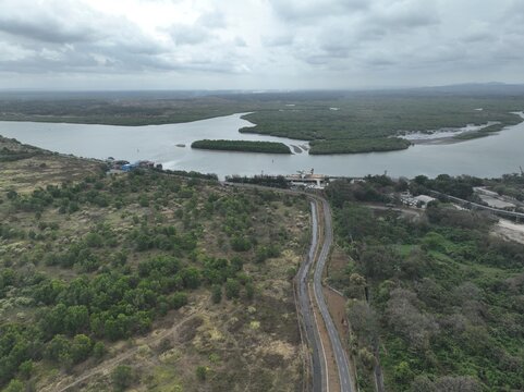 Aerial view of the coastal landscape and river estuary featuring lush mangrove forests and a winding road in Cilacap Regency, Central Java, Indonesia.