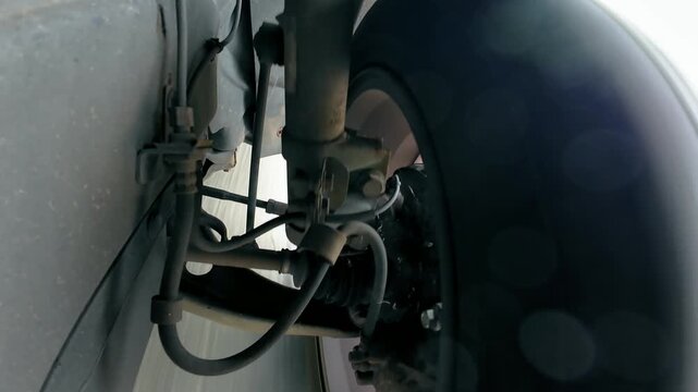 Car suspension working during road travel with wheel rotating beside shock absorber. Close underbody view of strut responding to vehicle motion. Steering linkage and brake components moving with