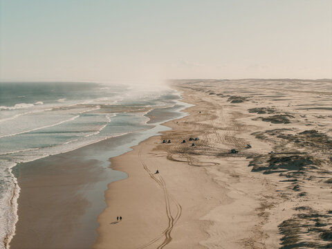 Aerial view of Birubi Point with expansive sand dunes, tire tracks from off-road vehicles, and gentle ocean waves washing onto the beach in Anna Bay, New South Wales, Australia.