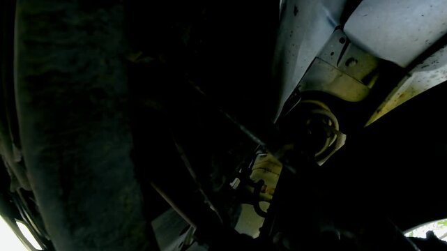 Steering and suspension components working beneath moving car during road travel. Tie rod shifting with wheel movement beside suspension mount. Close underbody perspective of front chassis and