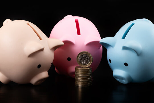 A 1 British pound coin and  colorful piggy banks on a black background.