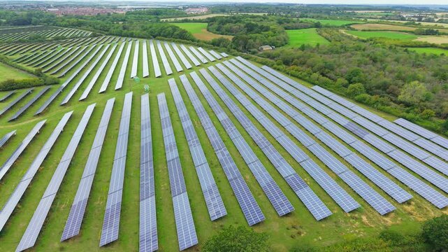 Solar panel farm across green countryside with rows of photovoltaic modules. Renewable energy infrastructure in rural landscape. Clean electricity generation from large scale solar power installation