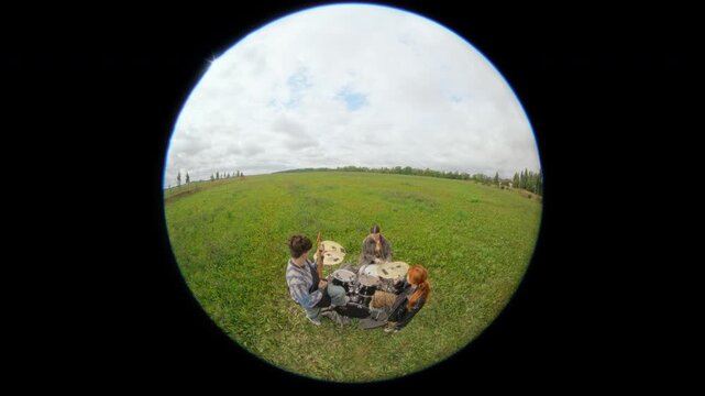 Gen Z Caucasian musicians playing drums and guitars in green field with fisheye lens. Visuals ideal for youth lifestyle marketing and indie band promotion
