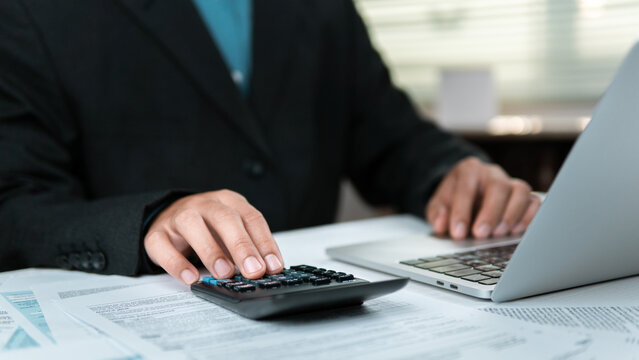 A businessperson is using a calculator, with documents and a laptop on the desk, to handle tax refunds and the preparation of financial reports for tax filing&mdash;streamlining processes and enhancing oper