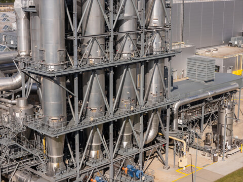 Aerial view of an industrial facility featuring large metal processing towers, complex piping systems, and steel support structures in Gdansk, Poland.