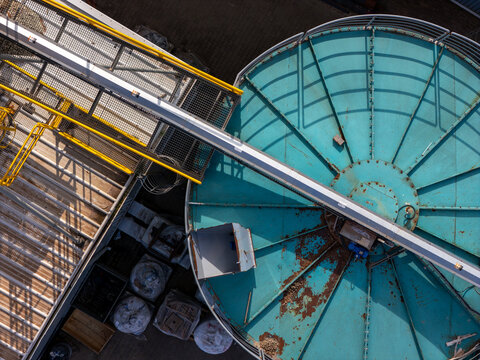 Aerial view of a large circular turquoise industrial tank with metal walkways and structural supports at a facility in Gdansk, Poland.
