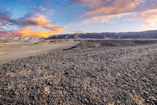 Vast arid desert landscape with rocky ground under golden sunset sky in Dahaidao, Xinjiang, China
