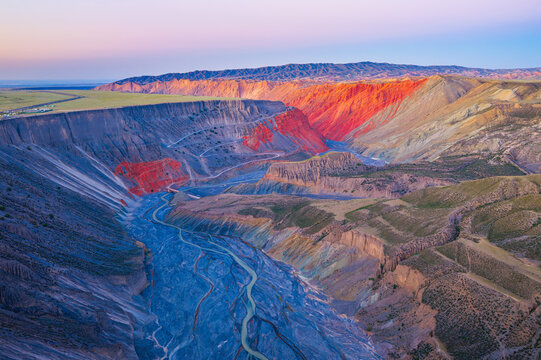 Aerial view of a deep gorge with a winding river and red cliffs at sunset in Anjihai Grand Canyon, Xinjiang, China