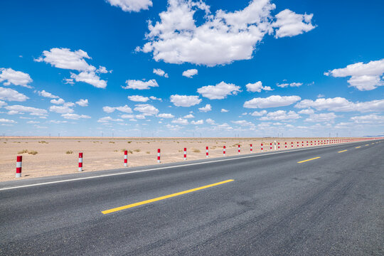 Empty straight asphalt highway stretching to the horizon through a desert landscape under a blue sky with clouds in Qinghai, China