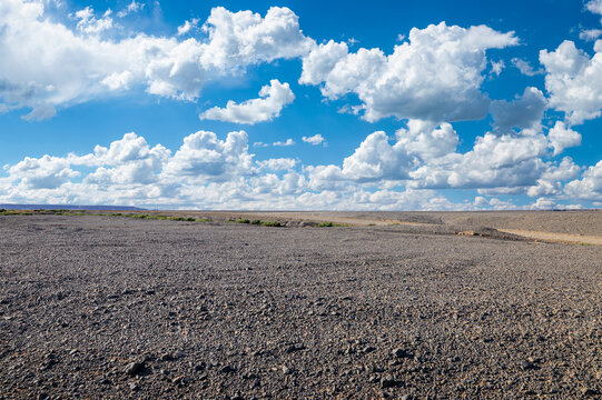 Vast gravel desert plain under a clear blue sky with white clouds in Xinjiang, China