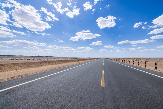 Empty straight asphalt highway stretching to the horizon through a desert landscape under a blue sky with clouds in Qinghai, China
