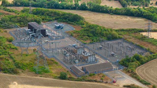 Aerial view of the Eaton Socon Substation 400kV featuring high-voltage power lines, transformers, and electrical infrastructure surrounded by rural fields in St. Neots, England, United Kingdom.