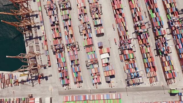 Top-down aerial view of a busy container port, showcasing rows of colorful shipping containers and large cranes used for loading and unloading cargo ships in the global supply chain