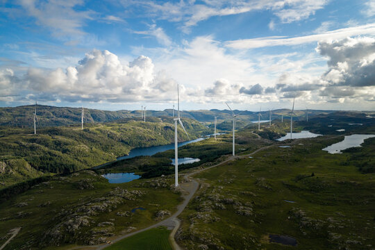 Aerial view of Makaknuten Vindkraftverk with wind turbines set against rolling green hills, lakes, and a blue sky with clouds in Bjerkreim Municipality, Rogaland, Norway.