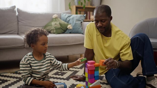 African American father and young child building colorful toy block tower on floor. Footage fits parenting commercials, early childhood education promos, and family lifestyle projects