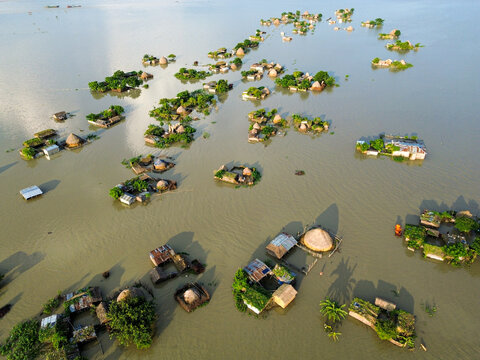 Aerial view of a rural village submerged by floodwaters, with houses on small elevated patches of land surrounded by murky water in Rajshahi District, Rajshahi Division, Bangladesh.