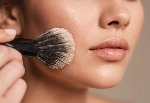 Close-up portrait of a woman applying face powder with a professional makeup brush for a natural glowing skin finish