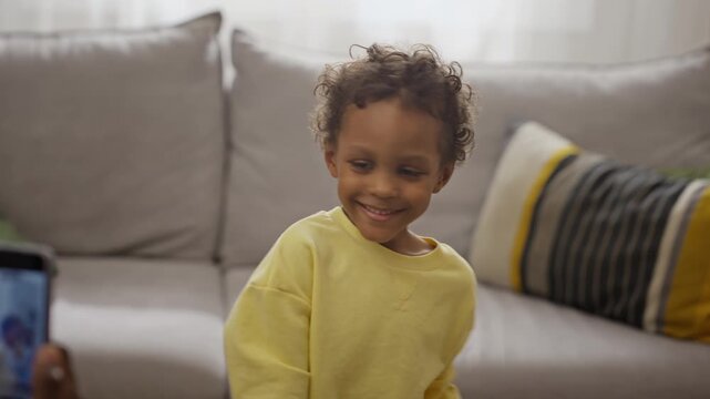 African American father filming smiling son playing with bubble gun using smartphone indoors. Footage suitable for parenting apps, mobile device advertising, and family lifestyle campaigns